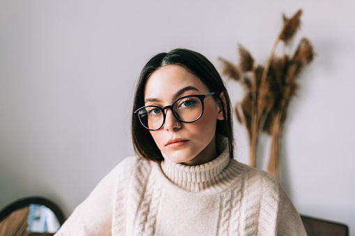 Authentic lifestyle portrait of pensive young caucasian woman in eyeglasses at home looking at camera.