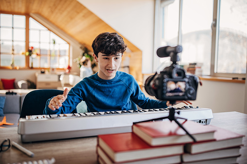 Two boys, cute modern boy making another music video playing synthesizer  for his audience with camera at home.