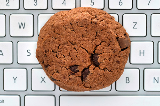 Brown cookie lies on a computer keyboard, as a symbol for data collection in the browser