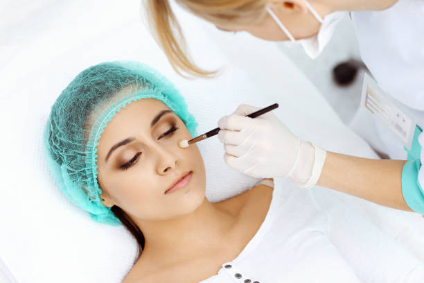 istock Professional beautician is doing cosmetic procedure at light medical background touching patient's face with brush, closeup. Cosmetology treatment 1301632369