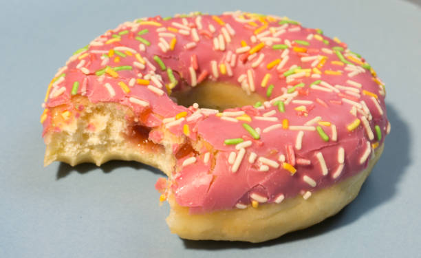 istock Pink doughnut or donut with colored sprinkles on a blue background. Bitten off American bagel. 1301637769