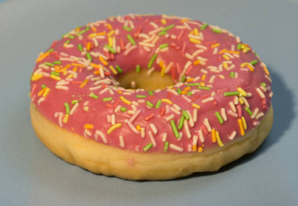 istock Pink doughnut or donut with colored sprinkles on a blue background. Bitten off American bagel. 1301638079