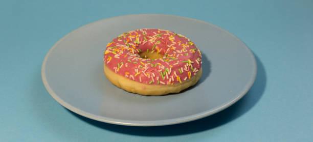 istock Pink doughnut or donut with colored sprinkles on a blue background. Bitten off American bagel. 1301638167