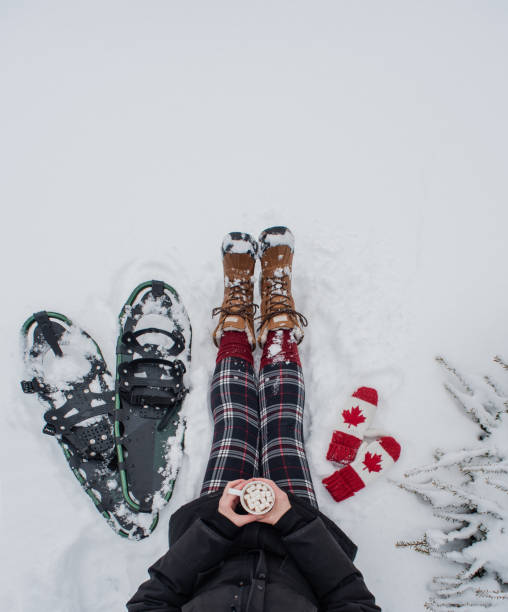 widok z góry kobieta siedząca w śniegu z rakietami śnieżnymi, rękawiczkami, gorącą czekoladą. - snowshoeing snowshoe women shoe zdjęcia i obrazy z banku zdjęć