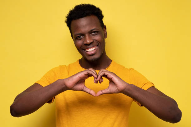 istock Handsome smiling young african man makes the heart using fingers on yellow wall. 1301639256