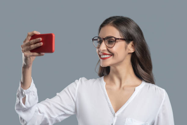 istock Woman with glasses holding smartphone at face level 1301640629