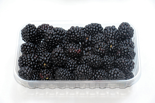 Fresh raw organic blackberries pile in plastic container isolated on white background