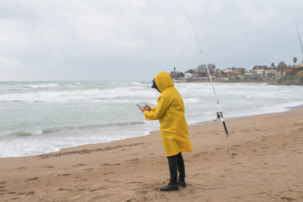 istock Fisherman using phone on the beach in bad weather 1301644020