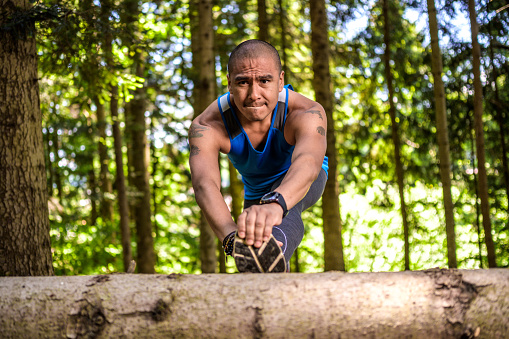 Man stretching his leg on tree trunk in forest.