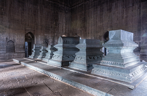 Vijayapura, Karnataka, India - November 8, 2013: Ibrahim Rauza Mausoleum. Closeup of row of several gray stone tombs in semi-dark room with only natural light.