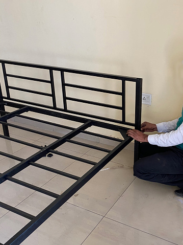 Stock photo showing an asian handy man assembling flat pack furniture metal bed frame.