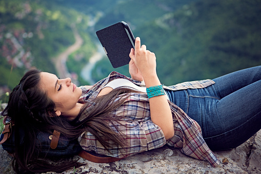 Young woman is reading e-book on edge of the cliff