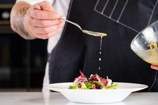 Chef finishing her plate and almost ready to serve at the table. The cook pours the salad from a spoon with sauce.