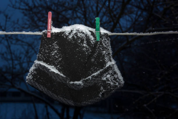A man's black hat hangs on a clothesline in winter after washing it is powdered with snow.