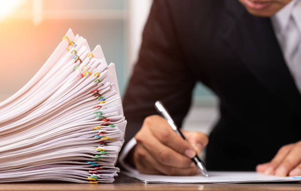 istock Male office workers holding and writing documents on office desk with light fair, Stack of business overload paper and paperless concept. 1301672926