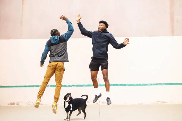 Photo of Two Generation Z Males Having Fun and Messing Around on a Hand Ball Court with Pet Dog Photo Series