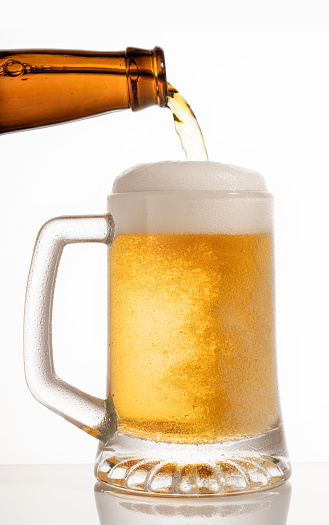 Golden beer being poured into a glass mug from a brown bottle.