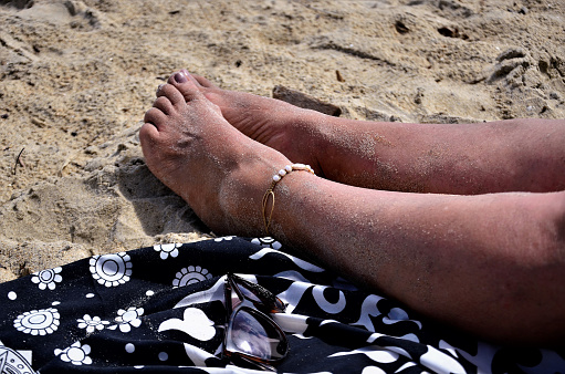 Legs relaxing on the sand on the beachside on the coast