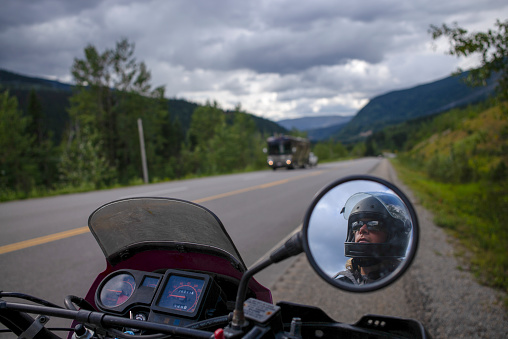 His face reflects in the side mirrors, he looks ahead, towards distant mountain range
