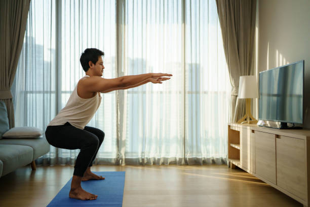Asian men exercise at home by squat in gym closures during COVID-19 outbreak.