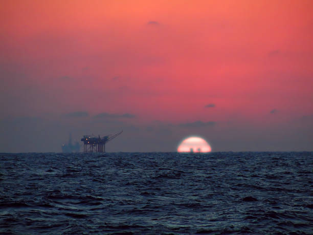 Oil Rig Sunset With oil rigs in the distance, the sun sets, turning the skies red over the choppy waters of the Gulf of Mexico. gulf of mexico photos stock pictures, royalty-free photos & images