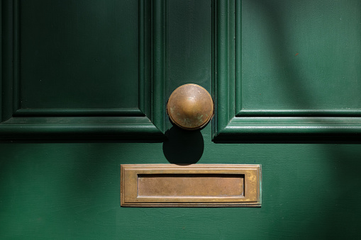 Closeup of an old wooden front door, with brass mail slot and knob..
