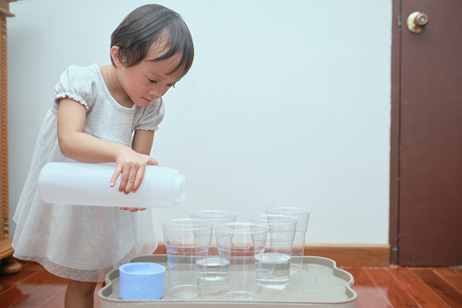 Cute Asian toddler girl having fun playing with water table at home, Wet Pouring Montessori Preschool Practical Life Activities, Fine Motor Skills development, Stay home Stay safe Have fun concept