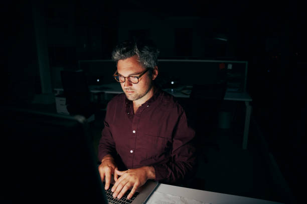 istock Businessman sitting in dark office room working on computer late at night 1301696415