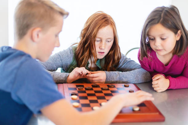 istock Three Siblings Playing checkers together at Dining Table Photo Series 1301702421