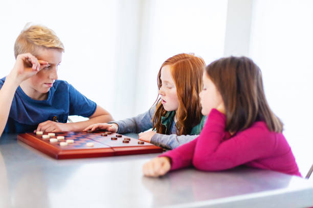 istock Three Siblings Playing checkers together at Dining Table Photo Series 1301702427