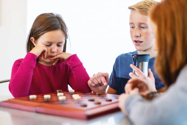 istock Three Siblings Playing checkers together at Dining Table Photo Series 1301702462