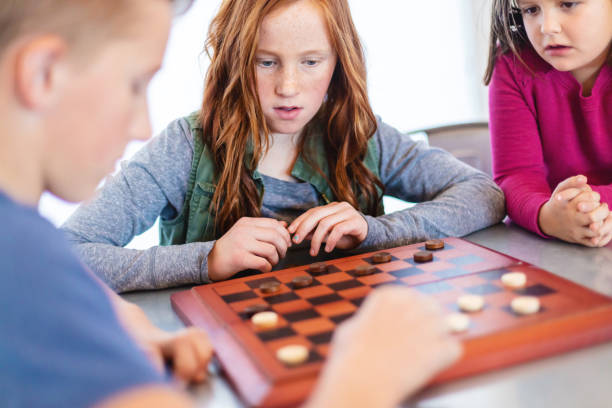 istock Three Siblings Playing checkers together at Dining Table Photo Series 1301702536