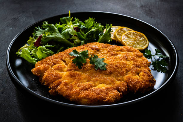 istock Fried pork chop with lemon and fresh vegetables on black table 1301707768