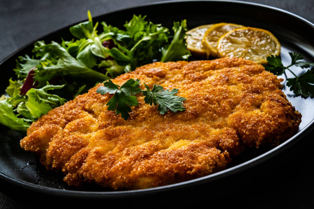 istock Fried pork chop with lemon and fresh vegetables on black table 1301707780