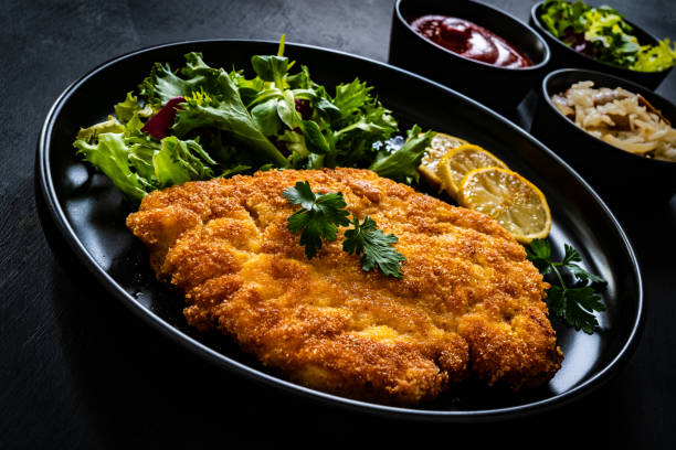 istock Fried pork chop with lemon and fresh vegetables on black table 1301707799