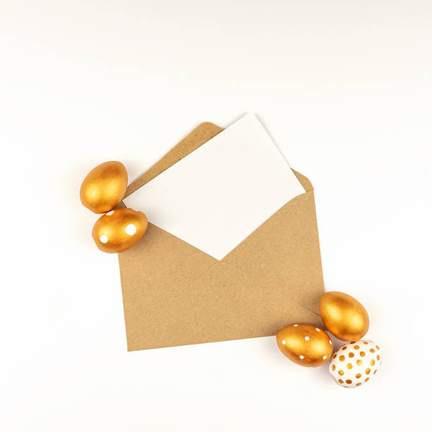 istock Easter festive decoration. Top view of easter eggs colored with golden paint and empty mock-up card in a kraft envelope. Various dotted designs. White background. 1301708435