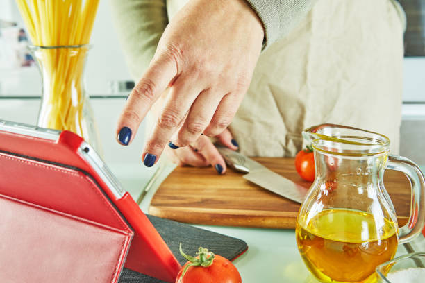 istock Woman use finger slide on tablet screen cooking according the tutorial of online virtual master class, And looking on the digital recipe, using touchscreen tablet while cooking healthy meal on the kitchen at home 1301708623