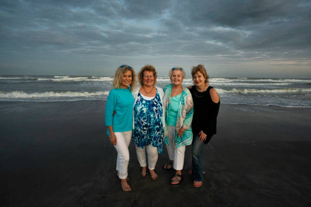 Women get away to Florida beach on winter break Senior woman and her three grown daughers stand on the sandy shore on a cold winter day, Cocoa Beach, Florida, USA cocoa beach photos stock pictures, royalty-free photos & images