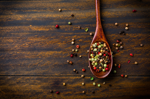 Colorful pepper corns in wooden spoon on wooden background