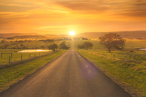 Sun setting on straight country road with farmlands, Milton, NSW, Australia