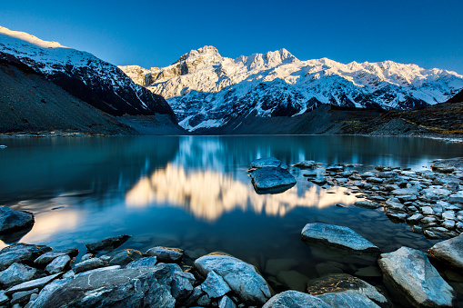 Early morning sun illuminating snow capped mountains with frozen lake in foreground, adventure in New Zealand.