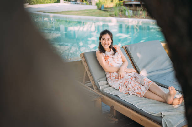 istock Young woman looking deep in thought and smiling while lying back in a deck chair on her patio on a sunny afternoon 1301716124