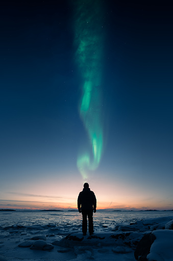 A man standing on the ice and looking at the sunset with Aurora above his head