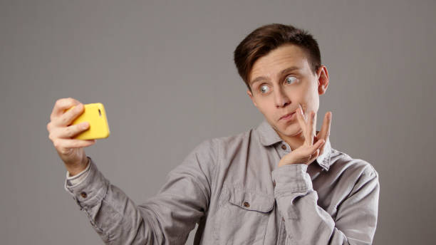 istock Caucasian man frowning taking selfie on mobile phone on grey background 1301716825
