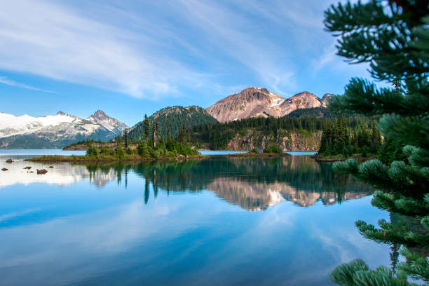 istock Pine trees mountains and bright blue sky reflecting on pristine lake 1301716890