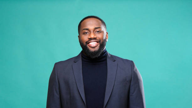 Sincere Afro American man in jacket smiles touching chest Sincere Afro American gentleman in turtleneck and jacket smiles showing white teeth touching chest by green studio wall closeup audition photos stock pictures, royalty-free photos & images
