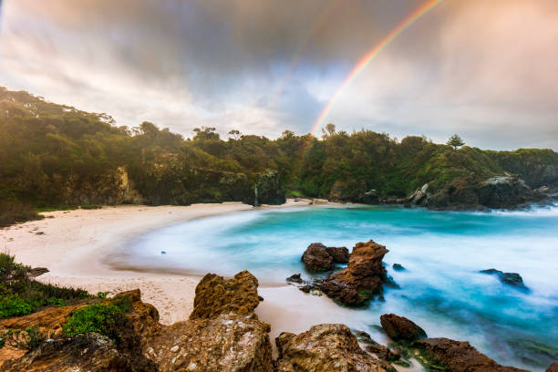 Beach cove with dramatic clouds forming a rainbow over the turquoise blue ocean
