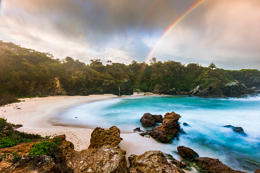 Beach cove with dramatic clouds forming a rainbow over the turquoise blue ocean, south coast, NSW, Australia