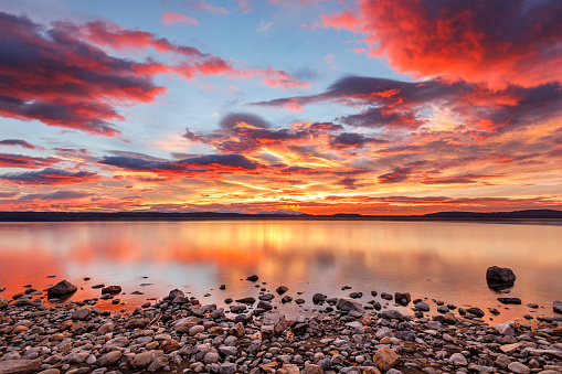 Bright red, orange and gold dramatic clouds at sunrise over lake in New Zealand