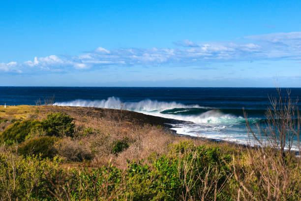 istock Large blue wave breaking off headland on clear blue sky day 1301719554